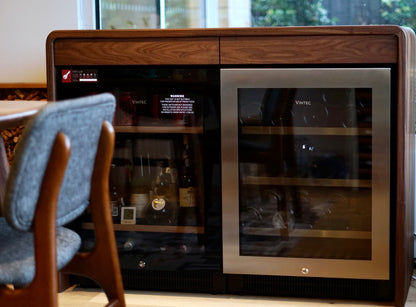 Wine cooler with bottles inside, placed in a room with chairs and a window in the background.